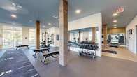 Located at 1804 Appaloosa Ln in Buford, GA, this generously sized fitness center spans a single floor and is thoughtfully divided into distinct workout zones, offering a comprehensive exercise experience. The space is anchored by striking wood-clad structural columns that add a warm, contemporary aesthetic against a crisp palette of white walls and a distinctive blue-painted ceiling.

The strength and cardio zone features rubber flooring, a power rack with weight plates, adjustable benches, a cable machine, treadmills, and an upright bike, all positioned to take advantage of large floor-to-ceiling windows that bathe the area in natural light and provide views of the surrounding outdoor greenery. A full-length mirrored wall with a dumbbell rack stocked with kettlebells and free weights enhances both functionality and the sense of openness.

Adjacent to the main gym floor is a dedicated functional training studio finished with light hardwood-style flooring. This area is equipped with a multi-functional training rig, resistance bands, medicine balls, punching bags, plyo boxes, and a turf sprint track. A wall-mounted flat-screen TV and large mirrors further elevate the space. The studio opens through glass-paneled doors to the strength area, creating a cohesive, flowing layout ideal for a wide range of fitness activities.