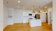 Located at 7015 Ruth Ave in Wilmington, NC, this well-appointed 2-bedroom, 2-bathroom single-floor home offers a clean, contemporary design throughout. The open-concept kitchen and living area serves as the heart of the home, showcasing white shaker cabinetry, a white quartz waterfall island with an undermount gold-toned sink, stainless steel appliances, a subway tile backsplash, and striking gold pendant lights that add a warm, modern touch. Light hardwood-style flooring flows seamlessly through the main living areas, enhancing the bright, airy atmosphere created by recessed lighting and natural light from multiple windows. The living area opens to a private balcony through a glass-paned door, offering outdoor views and additional natural light. Both bedrooms feature soft carpeting, ceiling fans, and ample natural light from windows with blinds. The generously sized primary bedroom connects to a dedicated closet. The bathrooms are finished in a clean, all-white palette with wood-look flooring, white vanities, and combination tub-shower units. A dedicated laundry area includes a full-size side-by-side washer and dryer with overhead shelving, adding everyday convenience to this thoughtfully designed home.