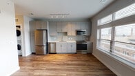 This single-floor unit offers a thoughtfully designed layout with modern finishes throughout. The kitchen serves as a standout feature, showcasing gray shaker-style cabinetry extending to the ceiling, a light glass subway tile backsplash, white quartz countertops, and a full suite of stainless steel appliances including a refrigerator, dishwasher, gas range, and microwave. Track lighting illuminates the space, while a large window with blinds allows generous natural light and urban views. The open layout connects the kitchen seamlessly to the living area, which features warm wood-tone luxury vinyl plank flooring and neutral wall tones.

The primary bedroom is bright and spacious, complete with a ceiling fan and the same wood-tone flooring. A second bedroom features plush carpet and a clerestory-style window for added light. Both rooms offer a clean, neutral palette ideal for customization.

The bathroom is finished in a crisp, all-white palette with large-format floor tiles, a soaking tub with a curved shower rod, recessed lighting, and a modern vanity. Completing the unit is a dedicated in-unit stacked washer and dryer, adding practical convenience to this well-appointed space.