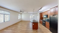 This single-story home offers a thoughtfully designed layout across three bedrooms and two bathrooms. The open-concept kitchen and living area serves as the heart of the home, featuring light wood-style flooring, neutral white walls, and multiple windows that allow natural light to fill the space. The kitchen is equipped with warm-toned wood cabinetry, black appliances including a range, oven, and refrigerator, a tile backsplash, and a central island with a dark granite countertop and built-in sink, illuminated by pendant lighting above. Track lighting provides additional task illumination. A ceiling fan in the living area adds comfort and function.

The bedrooms include the primary bedroom, which features wood-style flooring, two windows with outdoor views, and ample natural light, while additional bedrooms are finished with neutral carpet. Closets include sliding panel doors and a dedicated closet with a hanging rod for storage. The two bathrooms are consistent in finish, featuring warm wood cabinetry, granite-style countertops, and wood-style flooring. One bathroom offers a glass-enclosed shower, while the second includes a full shower-tub combination. A hallway connects the private areas of the home.
