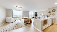 Located in the heart of downtown Dayton, this well-appointed 2-bedroom, 2-bathroom residence offers a thoughtfully designed open-concept layout with modern finishes throughout. The living, dining, and kitchen areas flow seamlessly together, anchored by expansive floor-to-ceiling windows that flood the space with natural light and frame sweeping views of the surrounding cityscape. Light-toned hardwood flooring runs throughout the main living areas, enhancing the bright and airy ambiance. The kitchen features a generous island with quartz countertops, white cabinetry with gold hardware, and stainless steel appliances, making it as functional as it is visually appealing. The dining area is defined by a striking geometric pendant light and large windows offering urban views. The spacious primary bedroom is outfitted with plush carpeting, a ceiling fan, and direct access to a private en-suite bathroom featuring marble-tiled walls and a glass-enclosed walk-in shower. A large walk-in closet with built-in shelving provides ample storage. The second bedroom is equally comfortable, served by a well-appointed hallway bathroom. Additional highlights include an in-unit laundry room and a dedicated hallway with closet access, completing this refined urban residence.