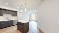 This thoughtfully designed residence at 2525 Via Alta in San Diego's Mission Valley area offers a modern, open-concept layout that seamlessly connects the kitchen and living room. The kitchen is a standout feature, showcasing dark espresso cabinetry, full-height storage, stainless steel appliances including a refrigerator, gas range, microwave, and dishwasher, along with a center island topped with light quartz countertops and stylish pendant lighting. Light wood-style flooring runs throughout the main living areas, enhancing the bright, airy atmosphere created by large windows that invite natural light. The living area provides access to a private balcony with pleasant outdoor views of the surrounding greenery. The bedroom is generously sized, featuring plush carpet flooring, a large window, and convenient access to a closet. The bathroom is clean and modern, featuring a full soaking tub with a shower, white tile surround, brushed nickel fixtures, and a dark wood medicine cabinet. Hallways connect the space efficiently, and the overall design palette of whites and neutrals lends a fresh, contemporary feel throughout.