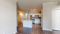 This single-floor residence offers a thoughtfully designed layout that balances open living with functional private spaces. The heart of the home is a well-equipped kitchen featuring crisp white cabinetry, a gray subway tile backsplash, light countertops, and a full suite of stainless steel appliances including a refrigerator, range, microwave, and dishwasher. A central island provides additional prep and casual dining space, while wood-look flooring ties the kitchen seamlessly into the adjacent living and dining areas. Crown molding and an arched architectural detail add a refined touch to the open-concept common areas, which benefit from natural light filtering in through the windows. A hallway connects the main living spaces to the private bedroom, which is finished with plush carpeting and direct access to a full bathroom. The bathroom features a vanity with storage, wood-look flooring, and a full tub-shower combination. An additional unfinished utility or flex room offers versatile potential. The residence also includes a spacious attached garage equipped with an automatic opener, providing generous storage and secure vehicle access. Throughout the home, neutral tones and consistent finishes create a clean, cohesive aesthetic.