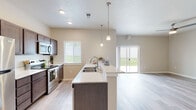 Located at 2641 Sunnyridge Rd in Nampa, Idaho, this two-story home presents a clean, modern design throughout its interior spaces. The open-concept main level centers around a well-appointed kitchen featuring dark espresso cabinetry, stainless steel appliances including a refrigerator, electric range, and over-the-range microwave, and a generous island with light quartz-style countertops and a double-basin sink. Pendant lighting suspended from the ceiling adds a polished touch above the island, while recessed lighting illuminates the space evenly. Light wood-style flooring flows seamlessly through the kitchen and into the adjoining living area, which benefits from abundant natural light and sliding glass doors that open to an outdoor view of the surrounding greenery. A ceiling fan enhances comfort in the living space.

The upper level features carpeted bedrooms, each with closets offering hanging storage. The bathrooms are finished with wood-look tile flooring, dark vanity cabinetry, light countertops, and tub-shower combinations with brushed nickel fixtures. Neutral wall tones throughout the home create a cohesive, understated palette. The overall ambiance is bright, functional, and move-in ready.