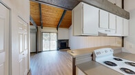 Located at 9310 E Montgomery Ave in Spokane Valley, WA, this efficiently designed single-floor unit offers a charming and functional layout across its compact footprint. The living room immediately impresses with vaulted ceilings clad in warm wood paneling, accented by exposed dark beams that lend a rustic character to the space. A stone-surround fireplace serves as a focal point, adding both visual interest and warmth, while a full-length sliding glass door floods the room with natural light and provides views of the surrounding greenery. White vertical board paneling along the walls and light wood-style flooring throughout create a clean, cohesive aesthetic. A baseboard heating unit ensures year-round comfort. The galley-style kitchen is thoughtfully appointed with white cabinetry, a coil-burner electric range, dishwasher, refrigerator, and overhead pendant lighting beneath the continued wood ceiling — maximizing functionality in a compact space. The walk-in closet offers generous built-in shelving and a full-length hanging rod, providing ample storage. The full bathroom features a combined tub and shower, a vanity with sink, and light, neutral finishes that maintain the unit's clean, understated design throughout.