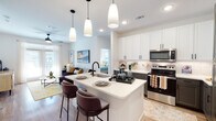 This single-floor residence is designed with a contemporary aesthetic, offering a cohesive open-concept layout that connects the kitchen, dining, and living areas seamlessly. The kitchen is a standout feature, equipped with two-tone cabinetry—white upper cabinets paired with charcoal lower cabinets—complemented by light quartz countertops, a subway tile backsplash, and a full suite of stainless steel appliances including a refrigerator with ice dispenser, range, and microwave. A central island with an undermount sink and matte black faucet provides additional prep space and bar seating beneath a trio of pendant lights.

The living area extends naturally from the kitchen, featuring light hardwood-style flooring, a ceiling fan, and large windows with french doors that allow ample natural light. Both bedrooms are carpeted and well-lit with natural light through large windows, each equipped with ceiling fans. The primary bedroom connects directly to a full bathroom featuring a dual-sink vanity with matte black fixtures, a wide mirror, and a tub-shower combination. The layout is efficient, bright, and finished with consistent modern detailing throughout.