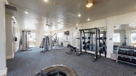 Located at 1701 Ennis Joslin Rd in Corpus Christi, Texas, this fitness center is a comprehensively equipped, single-floor facility designed to support a wide range of workout routines. The space features a clean, modern aesthetic with white walls, crown molding, and a combination of durable carpet tile and hardwood-style flooring throughout. Recessed lighting and ceiling fans provide ample illumination and airflow, while large windows along the perimeter flood the interior with natural light and offer views of the surrounding outdoor area, including a pool.

The cardio zone is well-stocked with elliptical trainers, treadmills, stair climbers, and a rowing machine, all positioned along the windowed wall to allow exercisers to take in the outdoor scenery. The strength training area includes a cable machine system, a Smith machine with an extensive weight rack, a dedicated free weight section with a full dumbbell rack and adjustable bench, and a leg extension/curl machine. Functional training is also supported, with a large tire, battle ropes, and stability balls available for dynamic workouts. Floor-to-ceiling mirrors are strategically placed to enhance the sense of space and support proper form. A wall-mounted television and organized storage cubbies add practical convenience to the well-rounded facility.