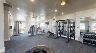 Located at 1701 Ennis Joslin Rd in Corpus Christi, Texas, this fitness center is a comprehensively equipped, single-floor facility designed to support a wide range of workout routines. The space features a clean, modern aesthetic with white walls, crown molding, and a combination of durable carpet tile and hardwood-style flooring throughout. Recessed lighting and ceiling fans provide ample illumination and airflow, while large windows along the perimeter flood the interior with natural light and offer views of the surrounding outdoor area, including a pool.

The cardio zone is well-stocked with elliptical trainers, treadmills, stair climbers, and a rowing machine, all positioned along the windowed wall to allow exercisers to take in the outdoor scenery. The strength training area includes a cable machine system, a Smith machine with an extensive weight rack, a dedicated free weight section with a full dumbbell rack and adjustable bench, and a leg extension/curl machine. Functional training is also supported, with a large tire, battle ropes, and stability balls available for dynamic workouts. Floor-to-ceiling mirrors are strategically placed to enhance the sense of space and support proper form. A wall-mounted television and organized storage cubbies add practical convenience to the well-rounded facility.