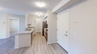 Located at 110-130 Edgar Lane in Sherwood Park, Alberta, this two-bedroom, two-bathroom unit offers a well-designed single-level layout with a clean, contemporary aesthetic. The open-concept living, dining, and kitchen area forms the heart of the unit, featuring light wood-look flooring, a textured ceiling, and a large window that invites natural light and views of the surrounding neighbourhood. The kitchen is appointed with granite-topped counters, a functional island with a double sink, light wood cabinetry, and a full suite of stainless steel appliances including a refrigerator, electric range with overhead microwave, and dishwasher. Both bathrooms share a consistent design language, each with granite vanity countertops, matching cabinetry, and a full tub-shower combination, complemented by wood-look flooring. The two bedrooms are carpeted for comfort, with windows providing natural light and neighbourhood views. Three closets offer generous storage throughout the unit. A dedicated laundry space houses a stacked front-load washer and dryer. The overall palette of white walls, neutral tones, and modern finishes creates a bright, functional, and move-in-ready living environment.