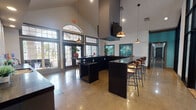 This single-story amenity facility is anchored by a striking clubroom defined by soaring vaulted ceilings that create an expansive, open atmosphere. Large arched transom windows and multi-pane glass doors flood the space with natural light, while polished concrete floors reflect the warm glow of copper pendant lights suspended overhead. The centerpiece of the clubroom is a substantial dark-topped bar, arranged in an L-shape configuration and surrounded by wood-and-metal bar stools, providing generous seating for gathering and socializing. A wall-mounted flat-screen television is positioned above a bold architectural hood element, adding a modern focal point to the room.

Adjacent to the main clubroom is a well-appointed kitchenette featuring dark granite countertops, a stainless steel double-basin sink, and modern cabinetry with textured gray fronts. A striking backsplash combines large white subway tiles with a contrasting black hexagonal mosaic accent band, adding a refined, contemporary detail. A microwave and beverage refrigerator are also integrated into the space.

The fitness center is comprehensively equipped with a full range of cardio machines—including treadmills, ellipticals, and stationary bikes—alongside a multi-station cable weight system, free weights, and exercise balls. Ceiling fans, wall-mounted televisions, and mirrored walls enhance the functionality and comfort of the workout area.