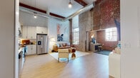 Located at 3315 N Davidson St in Charlotte's vibrant NoDa neighborhood, this single-floor loft masterfully blends industrial character with contemporary comfort. The open-plan living area commands attention with soaring ceilings, exposed ductwork, original timber beams, and dramatic exposed brick walls that stretch toward the ceiling. Large industrial-style windows flood the space with natural light, while light-toned hardwood flooring runs throughout, enhancing the airy feel.

The well-appointed kitchen features white cabinetry, a classic subway tile backsplash, stainless steel appliances including a French door refrigerator and dishwasher, and a functional layout that opens directly to the living space. A dedicated workspace nook is tucked alongside the exposed brick wall, offering a distinct work-from-home area with natural light from tall windows.

The bedrooms offer a quieter, more refined atmosphere with elevated ceilings, exposed wood beams, and tile flooring. The primary suite includes access to a spacious walk-in closet with full wire shelving systems. The bathroom is finished with a dual-sink vanity, black-framed mirrors, modern fixtures, and a glass-enclosed shower. An in-unit laundry area adds everyday convenience to this architecturally rich urban retreat.