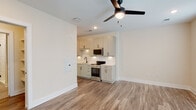 Located at 712 Halifax St in Raleigh, NC, this single-floor space offers a clean, modern design with thoughtful finishes throughout. The open-concept living and kitchen area is anchored by warm wood-look luxury vinyl plank flooring and recessed lighting, creating a bright and welcoming atmosphere. A ceiling fan overhead adds both functionality and style to the living space, which is bathed in natural light from dual windows dressed with white blinds.

The kitchen is efficiently laid out along one wall, featuring white shaker-style cabinetry with matte black hardware, white subway tile backsplash, light-toned countertops, and stainless steel appliances including a range and over-the-range microwave. A single-basin sink with a modern faucet completes the setup, while ample upper and lower cabinet storage ensures practicality.

A hallway connects the main living area to the private spaces beyond, including a well-appointed bathroom finished with large-format neutral floor tiles, a white vanity with matte black hardware, a toilet, and a walk-in glass-door shower with white tile surround. The overall palette of soft whites and warm neutrals throughout the space lends a cohesive, contemporary aesthetic that is both functional and visually inviting.