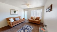 Located at 1777 W Orange Grove Rd in Tucson, Arizona, this single-floor residence offers a well-organized layout designed for comfortable everyday living. The living room is a welcoming, carpeted space featuring a ceiling fan, a large window with vertical blinds that allow ample natural light, and a sliding glass door that provides access to the outdoors. The adjacent dining area is defined by warm wood-look flooring and a pendant light overhead, creating an inviting atmosphere for meals and gatherings. The kitchen is efficiently arranged in an L-shaped configuration, featuring white cabinetry, dark countertops, a double-basin sink, and a full suite of appliances including a range and dishwasher. A window above the sink brings in additional natural light. The bedrooms are carpeted and restful, each offering closet storage — one bedroom features a spacious sliding-door closet with built-in shelving, while another includes a window with exterior views. The bathrooms feature wood-look flooring, with one showcasing a full tub-shower combination and another offering a vanity with a wide mirror and bright overhead lighting. Throughout, the neutral color palette and consistent finishes contribute to a cohesive and functional living environment.