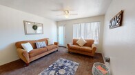 Located at 1777 W Orange Grove Rd in Tucson, Arizona, this single-floor residence offers a well-organized layout designed for comfortable everyday living. The living room is a welcoming, carpeted space featuring a ceiling fan, a large window with vertical blinds that allow ample natural light, and a sliding glass door that provides access to the outdoors. The adjacent dining area is defined by warm wood-look flooring and a pendant light overhead, creating an inviting atmosphere for meals and gatherings. The kitchen is efficiently arranged in an L-shaped configuration, featuring white cabinetry, dark countertops, a double-basin sink, and a full suite of appliances including a range and dishwasher. A window above the sink brings in additional natural light. The bedrooms are carpeted and restful, each offering closet storage — one bedroom features a spacious sliding-door closet with built-in shelving, while another includes a window with exterior views. The bathrooms feature wood-look flooring, with one showcasing a full tub-shower combination and another offering a vanity with a wide mirror and bright overhead lighting. Throughout, the neutral color palette and consistent finishes contribute to a cohesive and functional living environment.