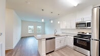 Located at 7112 Mechanicsville Turnpike in Mechanicsville, Virginia, this single-floor, 3-bedroom, 2-bathroom residence offers a clean, modern aesthetic with thoughtfully designed living spaces. The open-concept kitchen and living area serves as the heart of the home, featuring a central island with granite-style countertops, white shaker cabinetry, stainless steel appliances—including a refrigerator, range, microwave, and dishwasher—and stylish pendant lighting overhead. Light wood-style flooring flows throughout the main living areas, complementing the bright, neutral color palette. Two windows in the living area allow natural light to fill the space, creating an airy, welcoming atmosphere.

The primary bedroom is a comfortable, well-proportioned room with plush carpeting and a window providing natural light. Its en-suite bathroom features a dual-sink vanity with granite-style countertops, white cabinetry, and wood-style flooring. The two additional bedrooms also feature carpet and windows with exterior views. A second full bathroom includes a tub/shower combination with brushed nickel fixtures. The unit also includes a dedicated utility room and closet for added storage and functionality.