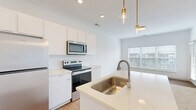 Located at 5155 Raglan St. in Hilliard, Ohio, this 1-bedroom, 1-bathroom residence offers a thoughtfully planned single-floor layout that maximizes every square foot. The open-concept kitchen serves as the heart of the home, showcasing a central island with an integrated sink and dishwasher, stainless steel appliances including a refrigerator, range, and microwave, and crisp white cabinetry paired with light countertops. Elegant gold-accented pendant lights hang above the island, adding a modern touch, while recessed lighting and light wood-style flooring enhance the bright, airy atmosphere. The living area flows seamlessly from the kitchen, grounded by plush carpeting that transitions into the bedroom. The bedroom is a comfortable retreat featuring soft carpet, clean white walls, and a generously sized window with blinds that invites natural light and outdoor views. A dedicated closet provides practical storage. The bathroom is finished with a sleek white vanity with an undermount sink, a framed mirror, warm wood-tone flooring, and a full tub-shower combo with built-in shelving. A private balcony rounds out the space, offering an outdoor extension ideal for fresh air and relaxation.