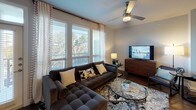 This single-floor residence offers a thoughtfully designed layout that balances functionality with modern style. The living room serves as the heart of the home, featuring large windows dressed with horizontal blinds and sheer curtains that flood the space with natural light while providing views of surrounding greenery. Dark hardwood-style flooring, a ceiling fan, and a glass-top coffee table contribute to the room's contemporary character.

The kitchen is equipped with stainless steel appliances, including a range, microwave, and refrigerator, complemented by white shaker-style cabinetry, light quartz countertops, and a decorative tile backsplash. Dark hardwood flooring continues throughout, adding cohesion to the open layout.

The primary bedroom is generously proportioned, featuring carpeted flooring, a ceiling fan, and a window with garden views. Its en-suite bathroom includes a dual-sink vanity with light countertops, a soaking tub, a separate shower, tile flooring, and direct access to a walk-in closet. The secondary bedroom also benefits from natural light and a ceiling fan, while its accompanying bathroom features a glass-enclosed shower and a modern vanity. Neutral tones and clean lines define the overall aesthetic throughout the residence.