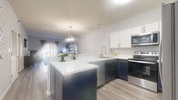 This thoughtfully designed single-floor residence offers 2 bedrooms and 3 bathrooms across a well-utilized footprint. The open-concept living area seamlessly connects the kitchen, dining, and living spaces, creating a bright and functional layout. The kitchen is a standout feature, showcasing two-tone navy and white cabinetry with gold hardware, sleek white quartz countertops, stainless steel appliances, a peninsula with bar seating, and a pendant light above — ideal for both cooking and entertaining. The dining area accommodates a round table and flows naturally into the living room, which features light wood-look flooring and sliding glass doors that open to an outdoor balcony or patio, allowing natural light to fill the space. Both bedrooms are carpeted and comfortably sized, with the primary bedroom offering a window with outdoor views and generous closet access. The second bedroom also includes a reach-in closet. Three bathrooms provide ample convenience, with one featuring a full tub-shower combo. A hallway bathroom doubles as a laundry room, housing a stacked washer and dryer unit alongside a vanity and toilet — maximizing efficiency. Throughout the residence, neutral tones and consistent finishes create a cohesive and inviting atmosphere.