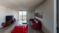 Located at 1355 Nicollet Ave in Minneapolis, MN, this high-rise unit offers sweeping panoramic views of the city skyline and surrounding neighborhoods through large floor-to-ceiling windows. The open-concept living area features durable wood-style flooring and is bathed in natural light, creating a bright and welcoming atmosphere. The living room provides generous space for lounging, while the adjacent dining area is anchored by an elegant chandelier overhead and connects seamlessly to the rest of the layout. The kitchen is outfitted with granite countertops, sleek gray cabinetry, a stainless steel farmhouse sink, a mosaic tile backsplash, and modern appliances — combining style with functionality. The unit includes two well-proportioned bedrooms, each featuring carpeted floors, ample closet storage with built-in shelving, and large windows framing impressive city views. The bathrooms are finished with clean, neutral tones; one features a tub-shower combination with tiled surround and granite countertop, while the other offers overhead cabinetry and brushed nickel fixtures. Throughout the unit, the neutral color palette and consistent finishes contribute to a calm, cohesive aesthetic suited for urban living.