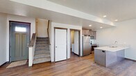 This two-floor space offers a practical and modern layout with clean finishes throughout. The main level centers around an open kitchen equipped with stainless steel appliances, including a refrigerator, electric range, and over-the-range microwave. Taupe-toned cabinetry pairs with light countertops and a white subway tile backsplash, while a peninsula with an undermount sink adds additional workspace and separation from the adjacent living area. Hardwood-style flooring runs throughout the main level, contributing to a cohesive and easy-to-maintain environment. A carpeted staircase connects the two floors, with access to additional rooms visible from the main level. The bedrooms are carpeted for comfort and each feature windows with blinds that provide natural light and neighborhood views. The bathrooms are finished with dark wood vanities, light countertops, subway tile backsplashes, and a walk-in shower enclosed by sliding glass doors. A dedicated laundry room houses a full-size washer and dryer alongside a water heater and furnace. The attached garage features a wide panel door with transom windows, offering ample parking and storage potential.