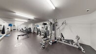 Located at 9675 Avenue Papineau in Montréal, QC, this fitness facility spans a single floor and is divided into two dedicated exercise rooms, offering a well-rounded environment for both cardio and strength training.

The space features a clean, modern aesthetic with white walls, durable rubber flooring, and bright fluorescent lighting that ensures excellent visibility throughout. A large wall-mounted mirror in the main exercise area enhances the sense of space and allows users to monitor their form during workouts.

The strength training zone is thoroughly equipped with a multi-station cable machine, a leg press and rowing machine combo, adjustable weight benches, and a full dumbbell rack with a wide range of free weights. Stability accessories, including a BOSU ball and exercise ball, are also available for functional training.

The cardio section houses a True treadmill, an elliptical trainer, a recumbent bike, and an upright stationary bike, catering to a variety of fitness levels and training preferences. A dedicated second room provides additional space for cardio equipment and is accessible via a glass-paneled door.

Overall, the facility is thoughtfully organized to maximize usability, maintaining clear floor space between equipment stations. The neutral color palette and efficient layout create a focused, functional atmosphere well-suited for regular fitness use.