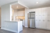 Located at 1867 Bloor St in Mississauga, Ontario, this two-bedroom, two-bathroom unit offers a well-organized single-floor layout designed for comfortable everyday living. The combined kitchen and living area serves as the heart of the home, where a sleek, modern kitchen stands out with white flat-panel cabinetry, a yellow tile backsplash, light quartz countertops, stainless steel appliances including a refrigerator, dishwasher, and range, and a central island providing additional prep and storage space. The open living area flows naturally from the kitchen, bathed in natural light through large windows that overlook the outdoors, with a sliding door providing access to a balcony. Wood-look laminate flooring runs throughout the unit, lending a warm, cohesive feel to every room. Both bedrooms are well-proportioned, featuring neutral tones, ample natural light, and dedicated closet space. The primary bedroom is generously sized with a window offering outdoor views and a baseboard heating unit. The two bathrooms are clean and functional — one featuring a full tub-shower combination with white subway tile surround and a vanity with mirror, and the other a straightforward powder-style layout. A hallway connects the rooms efficiently, completing this practical and neatly finished residence.
