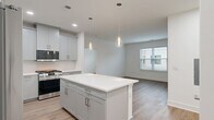Located at 300 Main Street in Madison, NJ, this thoughtfully designed two-bedroom, two-bathroom residence offers a bright and contemporary living experience across a single floor. The open-concept kitchen and living area serves as the heart of the home, anchored by a generous central island with crisp white quartz countertops. The kitchen is outfitted with soft gray shaker-style cabinetry, brushed nickel hardware, a herringbone tile backsplash, stainless steel appliances including a gas range and refrigerator, and elegant pendant lighting that adds a refined touch. Light wood-tone flooring runs seamlessly throughout, enhancing the clean, modern aesthetic. The living area receives natural light through large windows with views of the surrounding neighborhood. Both bedrooms are well-proportioned, featuring the same warm hardwood-style flooring, neutral walls, and windows that bring in natural light. The primary bathroom is particularly noteworthy, showcasing a double-sink vanity with quartz countertops, gold-toned hardware, large-format gray tile flooring, a frameless glass walk-in shower, and an expansive mirror. A dedicated closet provides added storage convenience. The overall ambiance is fresh, clean, and move-in ready, reflecting a modern design sensibility throughout.