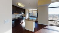 Located in Silver Spring, Maryland, this contemporary high-rise unit offers an impressive blend of modern design and urban convenience. The open-concept living area is defined by expansive floor-to-ceiling windows that wrap around the corner of the space, flooding the interior with natural light and framing sweeping panoramic views of the Silver Spring skyline. Rich hardwood flooring runs throughout the main living areas, adding warmth and elegance to the modern aesthetic.

The kitchen is thoughtfully designed with dark espresso cabinetry, granite countertops, a classic white subway tile backsplash, and a full suite of stainless steel appliances. A central island with a granite countertop provides additional prep space and connects seamlessly to the living area, making it ideal for both cooking and entertaining.

The bedrooms feature plush carpeting and large windows that continue the theme of abundant natural light and city views, with one bedroom offering direct access to a private balcony. The bathrooms are finished with coordinating dark cabinetry and granite countertops; the primary bath features a dual-sink vanity with a wide mirror and elegant fixtures, while the secondary bath mirrors the same refined style. This unit delivers a polished, urban living experience in a prime Silver Spring location.