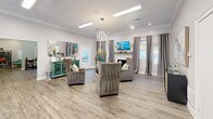 Located at 100 Bryton Trce in Columbia, SC, this thoughtfully designed single-story amenity space offers a generous layout across five distinct areas, all unified by durable wood-look flooring, crisp white trim, and a light, neutral color palette.

The welcoming hallway entry features a rich, wood-framed glass door, sage-green walls, crown molding, and recessed lighting, setting an inviting tone from the moment of arrival. The adjacent living room is a standout gathering space, furnished with plush wingback chairs, a decorative fireplace, a wall-mounted TV, and an ornate chandelier — all accented by crown molding and large windows with draping curtains that allow ample natural light.

The dining area transitions seamlessly into a workspace, boasting soaring vaulted ceilings with exposed beams and a shiplap finish, a modern pendant light, and windows offering outdoor views. A built-in reception counter anchors this zone, while a decorative ladder shelf adds a stylish touch.

The compact kitchen is efficiently appointed with white cabinetry, granite-look countertops, a stainless steel sink, and a full-size refrigerator — ideal for everyday convenience.

The exercise room is fully equipped with treadmills, ellipticals, a rowing machine, and a multi-use weight machine, all set against rubber flooring, full-wall mirrors, and motivational wall graphics, creating a functional and energizing fitness environment.