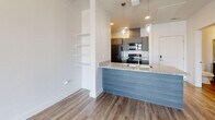 Located at 1905 S 300 W in Salt Lake City, Utah, this well-appointed one-bedroom, one-bathroom unit offers a thoughtfully designed layout across a single floor. The open-concept kitchen and living area serves as the heart of the home, featuring wood-look luxury vinyl plank flooring, a granite-topped breakfast bar peninsula with pendant lighting overhead, and built-in wall shelving for additional storage. The kitchen is equipped with dark wood cabinetry, granite countertops, and a full suite of stainless steel appliances including a refrigerator, electric range, microwave, and dishwasher. The bright living area flows seamlessly to a private balcony through sliding glass doors dressed with vertical blinds, inviting natural light throughout. The bedroom is finished with plush carpet, a window with outdoor views, and direct access to a dedicated closet featuring a full-width hanging rod and built-in lighting. The bathroom is appointed with rich navy cabinetry, granite countertops, a large vanity mirror, and a full tub and shower combination. Clean white walls, crisp trim, and consistent flooring choices lend a cohesive, contemporary feel to the entire space.