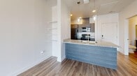 Located at 1905 S 300 W in Salt Lake City, Utah, this well-appointed one-bedroom, one-bathroom unit offers a thoughtfully designed layout across a single floor. The open-concept kitchen and living area serves as the heart of the home, featuring wood-look luxury vinyl plank flooring, a granite-topped breakfast bar peninsula with pendant lighting overhead, and built-in wall shelving for additional storage. The kitchen is equipped with dark wood cabinetry, granite countertops, and a full suite of stainless steel appliances including a refrigerator, electric range, microwave, and dishwasher. The bright living area flows seamlessly to a private balcony through sliding glass doors dressed with vertical blinds, inviting natural light throughout. The bedroom is finished with plush carpet, a window with outdoor views, and direct access to a dedicated closet featuring a full-width hanging rod and built-in lighting. The bathroom is appointed with rich navy cabinetry, granite countertops, a large vanity mirror, and a full tub and shower combination. Clean white walls, crisp trim, and consistent flooring choices lend a cohesive, contemporary feel to the entire space.