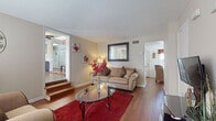 Located at 7000 Barrington Dr in Charlotte, NC, this two-floor home offers a well-organized layout with a variety of comfortable living spaces. The main living area features warm hardwood flooring, neutral-toned walls, and a split-level design with interior steps connecting to an adjacent room, adding architectural interest and a sense of depth. Natural light flows through the windows, enhancing the bright and airy feel throughout.

The kitchen is equipped with rich wood cabinetry, a tile mosaic backsplash, ample counter space, and black appliances, providing a functional and attractive cooking environment. Adjacent to the kitchen, the dining area accommodates a glass-top table with wicker chairs and benefits from natural light through a large window.

The home includes multiple bedrooms, each with plush carpeting and windows that invite natural light. The primary bedroom is generously sized, while additional bedrooms offer closet storage and comfortable proportions suitable for varied uses.

A cozy sitting area or den is also present, featuring hardwood floors and a window dressed with decorative curtains, offering a quieter retreat within the home. Overall, the space combines practical design with warm, inviting finishes throughout both floors.