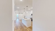 Located in Spring Hill, Tennessee, this thoughtfully designed single-story home offers four bedrooms and three bathrooms across a well-appointed open floor plan. Warm hardwood-style flooring flows throughout the home, complemented by crisp white walls and abundant natural light streaming through multiple windows.

The open-concept kitchen and living area serves as the heart of the home, featuring white shaker-style cabinetry, light quartz countertops, a large center island with an undermount sink and matte black faucet, stainless steel appliances, and pendant lighting. Board-and-batten wainscoting adds a refined farmhouse touch to the living and entry areas, while a sliding barn door accent contributes additional character.

The primary bedroom impresses with soaring vaulted ceilings, a ceiling fan, and a bright window framing outdoor views. Additional bedrooms are generously sized with vaulted or elevated ceilings, maintaining the home's airy feel. The bathrooms feature clean, all-white tub-shower combinations with matte black fixtures and built-in shelving niches.

A dedicated laundry room provides in-unit washer and dryer hookups with overhead shelving for storage. Two closets and a hallway complete the efficient layout, making this home as functional as it is stylish.