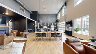 The Clubhouse at 4400 Calico Dr S in Fargo, North Dakota is a thoughtfully designed community space that seamlessly blends modern industrial aesthetics with warm, inviting elements. The single-floor layout offers a generous, open-concept footprint with soaring ceilings that amplify the sense of space and light throughout.

The main gathering area features light hardwood flooring, bold dark accent walls, and oversized pendant lighting suspended above a large communal dining table — ideal for events or casual gatherings. A fully equipped kitchen with stainless steel appliances, light wood cabinetry, white quartz countertops, open wood shelving, and dark tile backsplash provides excellent functionality for hosted events.

A dedicated lounge area includes a striking built-in electric fireplace framed by textured stone columns and flanked by leather armchairs, creating an intimate and cozy retreat within the larger space. Nearby, a curved, channel-tufted banquette seating area offers additional communal gathering space bathed in natural light from oversized windows.

A standout architectural feature is the full-panel glass garage door that opens to an outdoor patio, flooding the interior with natural light and providing a seamless indoor-outdoor connection. A wall-mounted television and media console round out the entertainment offerings. The overall ambiance is modern, sophisticated, and community-focused.
