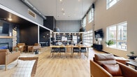 The Clubhouse at 4400 Calico Dr S in Fargo, North Dakota is a thoughtfully designed community space that seamlessly blends modern industrial aesthetics with warm, inviting elements. The single-floor layout offers a generous, open-concept footprint with soaring ceilings that amplify the sense of space and light throughout.

The main gathering area features light hardwood flooring, bold dark accent walls, and oversized pendant lighting suspended above a large communal dining table — ideal for events or casual gatherings. A fully equipped kitchen with stainless steel appliances, light wood cabinetry, white quartz countertops, open wood shelving, and dark tile backsplash provides excellent functionality for hosted events.

A dedicated lounge area includes a striking built-in electric fireplace framed by textured stone columns and flanked by leather armchairs, creating an intimate and cozy retreat within the larger space. Nearby, a curved, channel-tufted banquette seating area offers additional communal gathering space bathed in natural light from oversized windows.

A standout architectural feature is the full-panel glass garage door that opens to an outdoor patio, flooding the interior with natural light and providing a seamless indoor-outdoor connection. A wall-mounted television and media console round out the entertainment offerings. The overall ambiance is modern, sophisticated, and community-focused.