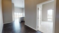 Located in Denver's vibrant RiNo district, this single-floor unit offers a contemporary design with soaring ceilings and neutral gray tones throughout. The open living area features dark hardwood flooring and large floor-to-ceiling windows that flood the space with natural light while framing elevated urban views of the surrounding cityscape.

The kitchen is well-appointed with crisp white cabinetry, dark countertops, a full suite of stainless steel appliances including a range, microwave, dishwasher, and refrigerator, complemented by stylish pendant lighting. A breakfast bar provides additional functionality at the kitchen's edge.

The bedrooms are carpeted for comfort and feature generously sized windows with city views and impressively tall ceilings that enhance the sense of space. Each room offers access to closet storage. The primary bedroom connects to an en-suite bathroom equipped with a glass-enclosed standing shower, dark wood-look flooring, light cabinetry, and a dark-topped vanity with an integrated sink. A second bathroom mirrors the modern aesthetic with a matching vanity and hardwood-style flooring. The overall design balances clean, modern finishes with a warm, livable atmosphere throughout.