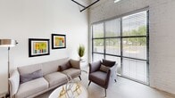 Located at 104 E Second St in Richmond, VA, this single-floor loft unit showcases a compelling blend of industrial heritage and contemporary design. Whitewashed exposed brick walls and soaring ceilings with visible ductwork and structural elements establish a distinctive loft aesthetic throughout the space.

The open living area is bathed in natural light from expansive floor-to-ceiling windows fitted with horizontal blinds, offering views of the surrounding neighborhood. Polished concrete floors flow seamlessly through the main areas, reinforcing the industrial character.

The kitchen is well-appointed with granite countertops, a white subway tile backsplash, white upper cabinetry, darker lower cabinets, and a full suite of stainless steel appliances. A compact dining nook with vibrant seating sits adjacent, making efficient use of the open layout.

Two bedrooms provide comfortable retreats, with one featuring a whitewashed brick accent wall complete with a distinctive arched architectural detail, adding a sense of historic depth. A dedicated office nook with clerestory windows above offers a bright, focused workspace.

Two bathrooms serve the unit, both finished with white cabinetry and dark granite countertops. The primary bath features dual vessel sinks, while the secondary bath includes a full tub-shower combination. The overall ambiance is one of urban sophistication rooted in Richmond's architectural history.