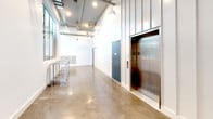 Located at 3008 Santa Monica Blvd in Santa Monica, CA, this single-story building combines contemporary design with functional, well-appointed common areas. The lobby makes an immediate impression with its striking floor-to-ceiling vertical slat wall panel feature, polished concrete floors, and a geometric pendant light fixture that casts warm ambient lighting throughout the entry. Large windows allow natural light to filter in, creating a bright and welcoming atmosphere.

Moving deeper into the building, wide corridors with soaring ceilings and exposed ductwork and piping lend an industrial-modern character to the space. Pendant globe lights hang at intervals along the hallways, providing consistent illumination. The polished concrete flooring continues throughout, offering a cohesive and durable finish.

A stainless steel elevator provides convenient access and serves as a notable architectural element, framed by vertical steel paneling. Nearby, a comprehensive bank of individual mailboxes is recessed into the wall, accommodating a significant number of occupants. Additional utility spaces and access doors are neatly integrated along the corridors. The overall design balances clean, minimalist aesthetics with practical infrastructure, making this a well-designed and functional commercial or mixed-use building.