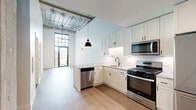Located at 4715 West Irving Park Road in Chicago's Irving Park neighborhood, this one-bedroom, one-bathroom residence blends modern design with industrial-chic character. The open layout is anchored by light hardwood flooring and soaring ceilings that lend a spacious, airy feel throughout. Exposed structural elements, including steel beams and translucent ceiling panels, add an industrial aesthetic that sets the space apart.

The kitchen is a standout feature, showcasing white shaker cabinetry, a classic subway tile backsplash, and a striking granite peninsula countertop ideal for dining or entertaining. Stainless steel appliances — including a gas range, built-in microwave, dishwasher, and French door refrigerator — complete the well-appointed culinary space. A bold black pendant light hangs overhead, adding a contemporary accent.

The living area benefits from floor-to-ceiling windows and direct access to a private balcony, flooding the room with natural light and offering open views of the surrounding neighborhood. The bedroom is a bright, clean retreat with generous proportions and easy access to the hallway.

The bathroom is thoughtfully designed with a deep navy vanity, marble-look granite countertop, dark mosaic tile flooring, and a walk-in glass-enclosed shower with crisp white tile surround and matte black fixtures — a refined, modern finish throughout.