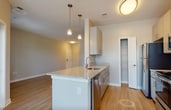 Located at 9755 Mill Centre Dr in Owings Mills, MD, this single-floor residence offers a thoughtfully designed open-concept layout with contemporary finishes throughout. The kitchen serves as the heart of the space, anchored by a granite-topped peninsula island with an undermount sink and pendant lighting above. It is fully equipped with stainless steel appliances, including a refrigerator, range, microwave, and dishwasher, complemented by light-toned cabinetry and light hardwood-style flooring that flows seamlessly into the adjoining dining and living areas. The dining area benefits from multiple windows offering views of the surrounding greenery, filling the space with generous natural light. The living room is similarly bright, featuring hardwood-style flooring and a clean, neutral palette. The bedroom is a spacious, carpeted retreat with a large window that frames lush outdoor views, accompanied by a generously sized walk-in closet outfitted with wire shelving and hanging rods for ample storage. The bathroom includes a full tub-shower combination, a vanity with under-sink cabinetry, and a large mirror. Throughout the unit, warm neutral tones, clean lines, and consistent modern finishes create a cohesive and inviting living environment.