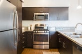 Located on Rogers Drive in Goleta, California, this single-story unit offers a well-designed layout with a cohesive mix of modern finishes and functional living spaces. The open-concept kitchen serves as a central highlight, featuring dark espresso cabinetry, granite countertops, stainless steel appliances, and a peninsula island with pendant lighting above. Wood-look flooring runs throughout the main living areas, lending warmth and visual continuity, while a ceiling fan accents the living space, which connects directly to a private balcony via sliding glass doors—bringing in natural light and outdoor views of the surrounding neighborhood.

The bedrooms are carpeted for comfort, each equipped with ceiling fans and window blinds that allow for adjustable natural light. One bedroom includes a mirrored sliding-door closet with built-in shelving and a hanging rod, offering practical storage. The bathroom presents a double-sink vanity with granite countertops, dark wood cabinetry, and chrome hardware, maintaining the refined aesthetic found throughout the unit. In-unit laundry is also available, visible through louvered closet doors near the kitchen. The overall ambiance is clean, neutral, and move-in ready.