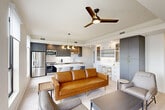 Located at 3100 Lake Villa Dr in Metairie, Louisiana, this modern 2-bedroom, 1-bathroom residence offers a thoughtfully designed open-concept layout. The combined dining, kitchen, and living area forms the heart of the home, bathed in natural light from large black-framed windows that frame expansive views of the Metairie skyline. The kitchen is a standout, featuring two-tone cabinetry in charcoal and warm wood tones, gold hardware accents, quartz countertops, stainless steel appliances, and a central island with seating. A sculptural multi-globe pendant light adds a refined touch overhead. The living area flows seamlessly from the kitchen, complemented by a ceiling fan and direct access to a private balcony with panoramic outdoor views. A built-in workspace with white cabinetry and shelving provides a dedicated functional nook. Both bedrooms are bright and serene, with light wood-style flooring, ceiling fans, and large windows offering outdoor views. The primary bedroom includes dedicated closet space. The bathroom is elegantly appointed with marble-look tile flooring, a glass-enclosed walk-in shower with matching tile surround, a wood vanity with gold accents, and a round mirror. Additional conveniences include in-unit laundry, hallway storage, and multiple closets throughout.