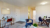 This single-floor residence offers a thoughtfully designed layout that balances comfort and functionality. The open living area is generously sized, featuring soft carpeting, neutral wall tones, and a bright window that draws in natural light and provides views of the surrounding neighborhood. The space accommodates a full seating arrangement with ease, creating a welcoming environment for relaxing or entertaining.

Adjacent to the living area is a dedicated dining nook, sized comfortably for a round dining table and chairs — ideal for everyday meals or casual gatherings. The kitchen is outfitted with white shaker-style cabinetry, a classic subway tile backsplash, light countertops, and stainless steel appliances including a gas range and over-the-range microwave. Light wood-style flooring and a matte black faucet add modern contrast to the bright, clean aesthetic.

The bedroom is a calm retreat, featuring carpet flooring, a large window with blinds for natural light and privacy, and a closet with louvered doors. The layout connects smoothly back to the main living space. The bathroom is finished with neutral tile flooring and includes a shower-tub combination, maintaining a clean and functional design consistent with the rest of the residence.