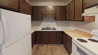 Located at 118 Broadhurst Rd in Jacksonville, NC, this single-floor home offers a practical and straightforward layout designed for comfortable everyday living. The living area is spacious and carpeted, featuring vertical wood-paneled walls, a textured ceiling, and a ceiling fan with overhead lighting. Natural light filters in through windows dressed with horizontal blinds, and a warm wood-toned entry door adds character to the space.

The kitchen is well-equipped with an abundance of dark wood cabinetry providing generous storage above and below the countertops. A double-basin stainless steel sink sits at the center, flanked by countertop workspace. White appliances, including a refrigerator and range, complete the functional setup, while wood-look vinyl flooring adds a clean, durable finish underfoot.

The bedroom continues the carpeted flooring and paneled wall aesthetic, offering a quiet and comfortable retreat with a window providing natural light. A wood-paneled door leads to the closet, maintaining the cohesive design of the space.

The bathroom features wood-look vinyl flooring and includes a full tub and shower combo with a molded surround, a toilet, and a vanity with sink. Towel bars and a textured ceiling round out this utilitarian yet tidy space. Overall, the home presents a consistent, functional design throughout its single floor.