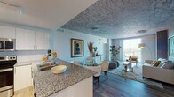 Located at 2160 Van Burden Street in Hollywood, Florida, this apartment on the sixth floor offers a thoughtfully designed open-concept layout with modern finishes throughout. The kitchen is outfitted with stainless steel appliances, white cabinetry, granite countertops, and a breakfast bar that flows seamlessly into the dining and living areas. A distinctive textured ceiling adds an artistic, elevated character to the main living spaces, complementing the light-toned hardwood flooring below. The living room is bathed in natural light from expansive floor-to-ceiling windows that open to views of the surrounding Hollywood skyline and beyond, with access to an outdoor balcony. The primary bedroom is generously proportioned, featuring the same decorative textured ceiling, ample closet space, and bright windows. A second bedroom provides additional flexibility. The primary bathroom is finished with a double granite-topped vanity, backlit mirrors, and clean tile flooring, while the secondary bathroom features a tub-shower combination with elegantly tiled walls and a granite vanity. Track lighting in the kitchen and contemporary fixtures throughout complete the refined, modern aesthetic of this well-appointed Hollywood residence.