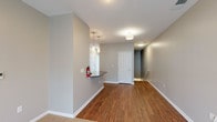 This single-floor unit is designed with a clean, contemporary aesthetic defined by neutral gray walls, white trim, and warm hardwood flooring that flows throughout the main living areas. The open layout connects a generously sized living space to a kitchen equipped with stainless steel appliances, including a side-by-side refrigerator with ice and water dispenser, an electric range, and an over-the-range microwave. White shaker-style cabinetry reaches toward the ceiling, offering substantial storage, while dark granite countertops and a white subway tile backsplash add a polished contrast. A pass-through counter provides a convenient transition between the kitchen and living area. Pendant lighting and flush-mount fixtures illuminate the main spaces effectively. Bedrooms feature plush neutral carpet and ample wall space, providing a quiet retreat. The bathrooms are finished consistently with white vanity cabinetry, dark granite countertops, and hardwood-style flooring; the primary bathroom includes a glass-enclosed shower and a large mirror with overhead lighting. A dedicated utility area houses a stacked washer and dryer unit for added convenience. Overall, the space presents a well-appointed, move-in-ready interior with cohesive finishes throughout.