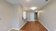 This single-floor unit is designed with a clean, contemporary aesthetic defined by neutral gray walls, white trim, and warm hardwood flooring that flows throughout the main living areas. The open layout connects a generously sized living space to a kitchen equipped with stainless steel appliances, including a side-by-side refrigerator with ice and water dispenser, an electric range, and an over-the-range microwave. White shaker-style cabinetry reaches toward the ceiling, offering substantial storage, while dark granite countertops and a white subway tile backsplash add a polished contrast. A pass-through counter provides a convenient transition between the kitchen and living area. Pendant lighting and flush-mount fixtures illuminate the main spaces effectively. Bedrooms feature plush neutral carpet and ample wall space, providing a quiet retreat. The bathrooms are finished consistently with white vanity cabinetry, dark granite countertops, and hardwood-style flooring; the primary bathroom includes a glass-enclosed shower and a large mirror with overhead lighting. A dedicated utility area houses a stacked washer and dryer unit for added convenience. Overall, the space presents a well-appointed, move-in-ready interior with cohesive finishes throughout.