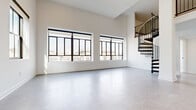 Located in the heart of downtown Columbus at 70 N High St, this two-story residence offers a thoughtfully designed layout spread across two generous floors. The main level provides an expansive open-concept living area bathed in natural light through large, black-framed windows that frame views of the surrounding urban streetscape. A striking spiral staircase anchors the space, serving as both a functional and architectural focal point.

The kitchen is well-appointed with dark cabinetry accented by gold hardware, a subway tile backsplash, stainless steel appliances, and a large center island with a crisp white quartz countertop — ideal for both cooking and entertaining.

The upper floor features soft carpeting throughout, with the generously sized primary bedroom offering a dedicated walk-in closet with wire shelving systems and a private en-suite bathroom. The primary bath includes a dual-sink vanity with dark cabinetry, white quartz countertops, and a tiled walk-in shower with black-framed glass doors. A second full bathroom features a tiled tub-shower combination with matte black fixtures. Additional bedrooms are bright and carpeted, each with windows overlooking the city. The residence also includes a utility room and ample hallway circulation space across both floors.
