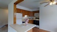 Located at 800 Kimberton Road in Phoenixville, Pennsylvania, this single-floor residence offers a practical and welcoming layout designed for comfortable everyday living. The kitchen is a standout feature, showcasing warm honey-toned wood cabinetry that lines the walls from counter to ceiling, providing generous storage throughout. A full suite of appliances is included, featuring a black electric range, built-in microwave, and a full-size white refrigerator. Light-toned countertops complement the cabinetry and extend to a peninsula-style breakfast bar, which opens the kitchen toward the adjacent living area — creating a connected, social atmosphere. The pass-through framing, accented with a rustic wood beam overhead, adds a touch of architectural character to the space. Hardwood flooring runs through the kitchen, contributing warmth and continuity to the interior. The single-floor layout ensures ease of navigation throughout the home, making it an accessible and efficient living environment. The overall ambiance is cozy and functional, with a classic residential aesthetic that balances practicality with homey charm, well-suited for those seeking a comfortable and straightforward living space in the Phoenixville area.