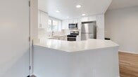 Located at 12700 Bloomfield Ave in Norwalk, CA, this one-bedroom, one-bathroom residence offers a thoughtfully designed single-floor layout with modern updates throughout. Light-toned wood-style flooring runs through the living areas, complementing the neutral wall palette and creating a clean, cohesive aesthetic.

The kitchen is a standout feature, showcasing white shaker cabinetry, bright white quartz countertops, recessed lighting, and a peninsula that opens to the adjacent dining area. Stainless steel appliances — including a gas range, over-the-range microwave, and refrigerator — complete the well-appointed space. A window above the sink brings in natural light.

The living room is open and airy, featuring a sliding glass door fitted with vertical blinds that leads to one of two private balconies, offering views of surrounding greenery. The dining room similarly connects to outdoor space via a second balcony.

The bedroom is a comfortable size, featuring its own closet with built-in shelving, wood-style flooring, and direct hallway access to an additional closet. The bathroom is finished with white cabinetry, quartz countertops, wood-style flooring, and a full shower-tub combination with chrome grab bars. A dedicated laundry area and a hallway complete the floor plan, adding everyday practicality to this well-organized residence.